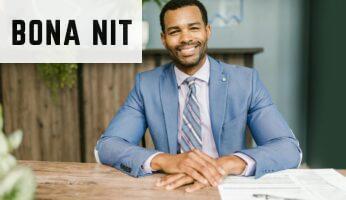Smiling businessman in office attire sitting at a desk with documents.