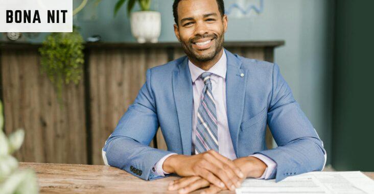 Smiling businessman in office attire sitting at a desk with documents.