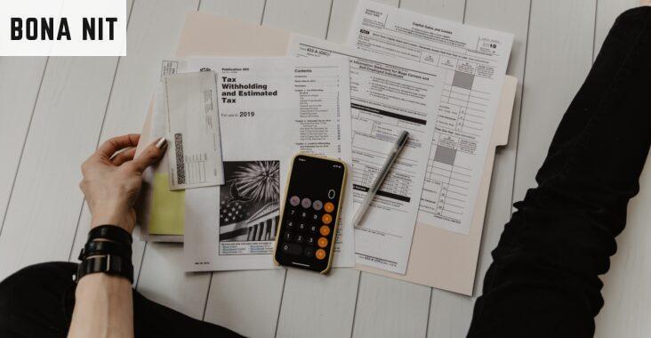 person holding paper near pen and calculator